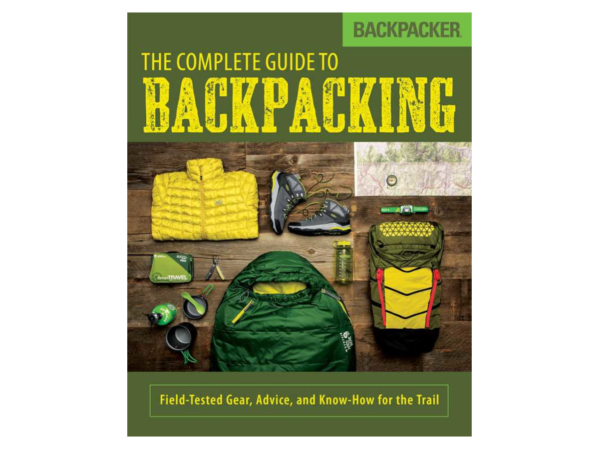 Book cover of 'The Complete Guide to Backpacking' with backpacking gear on a wooden background