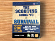 Book titled 'The Scouting Guide to Survival' on a wooden surface